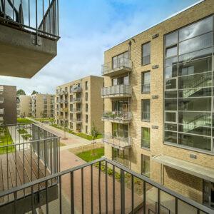 Blick vom Balkon einer Wohnung auf viergeschossiges Wohnhaus mit sandfarbenem Klinker und Balkons