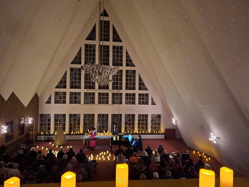 Querflötenspielerin in rotem Kleid mit Klavierbegleitung in stimmungsvoller Kirchenatmosphäre, umgeben von Kerzen
